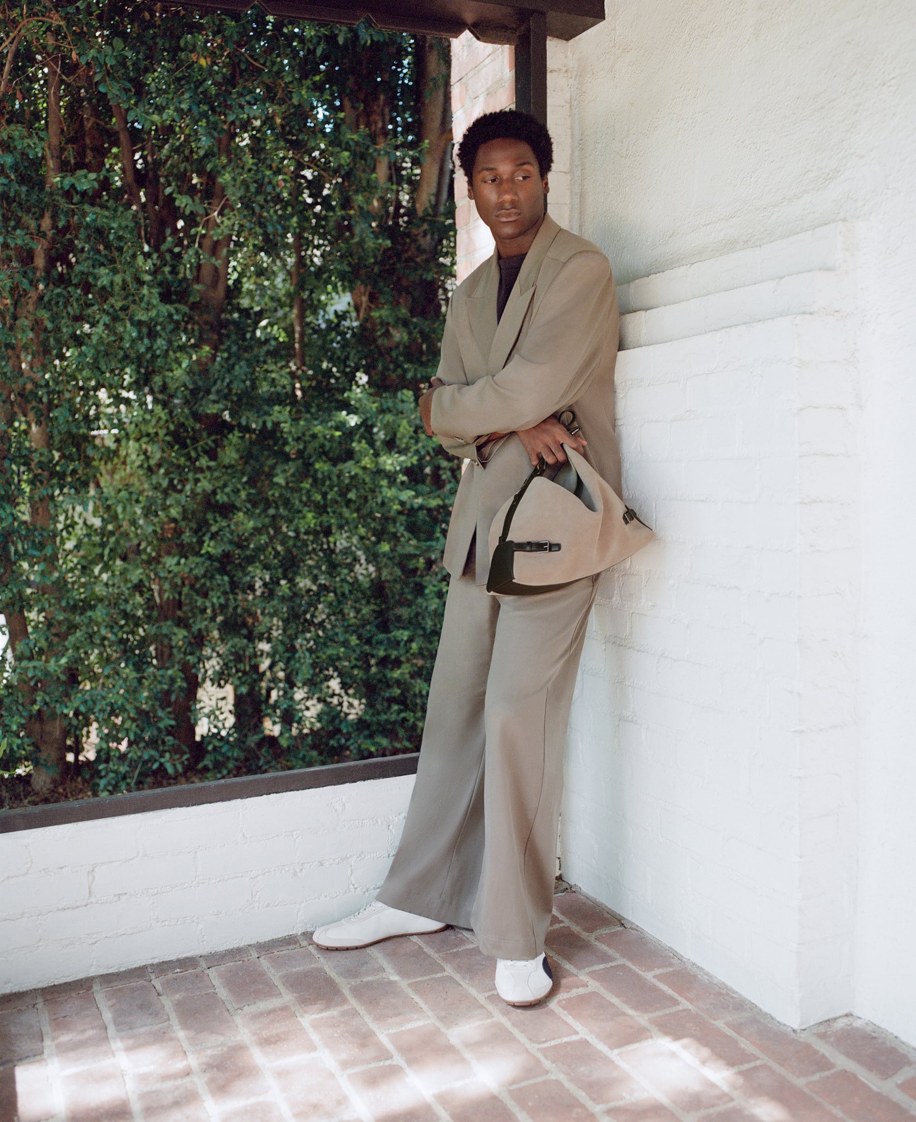 Jabari Wimbley in a beige suit leaning against a white brick wall