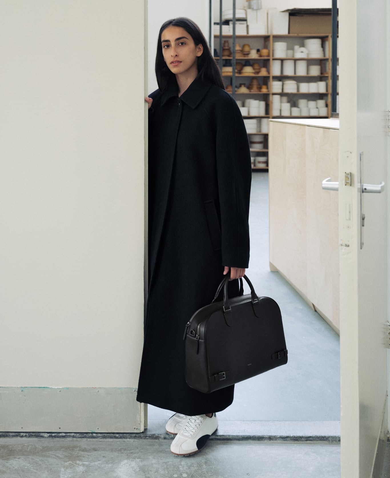 Tahni Bouhadana in a long black coat holding a black PEDRO bag