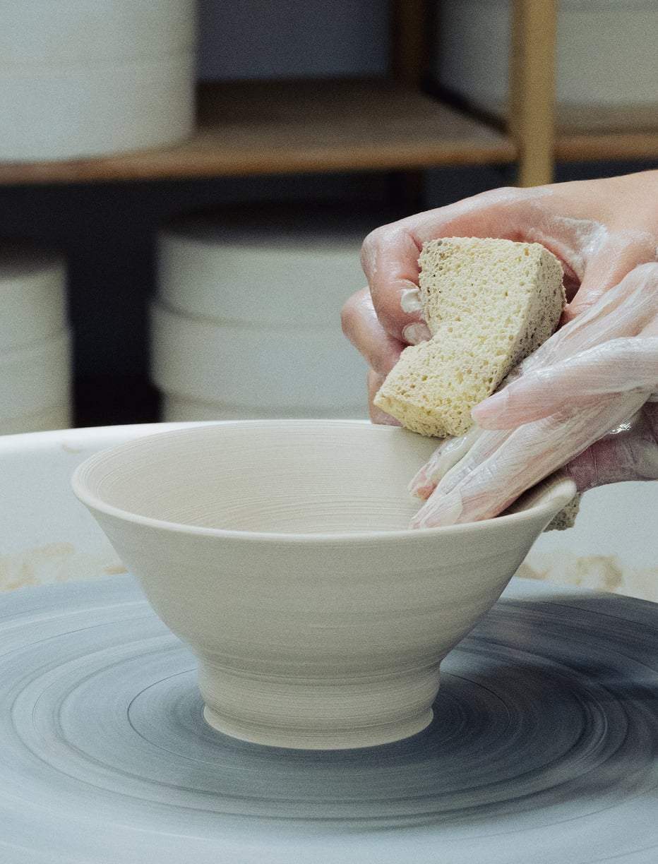 Hands shaping a clay bowl on a pottery wheel