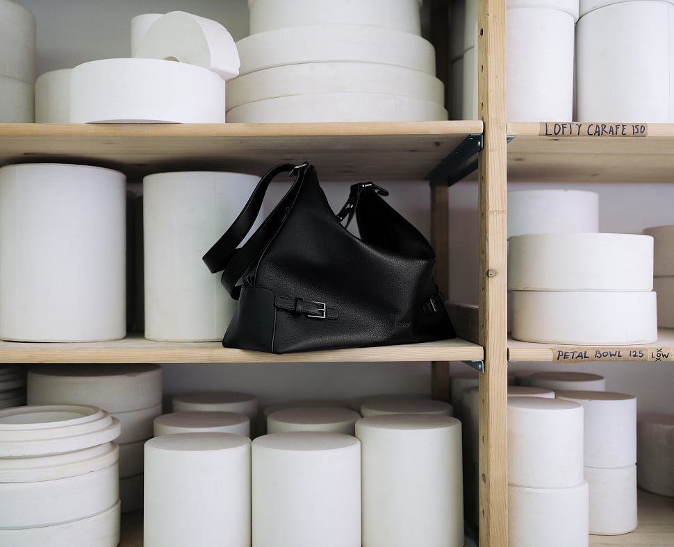 A black PEDRO bag on a shelf among white ceramic vessels