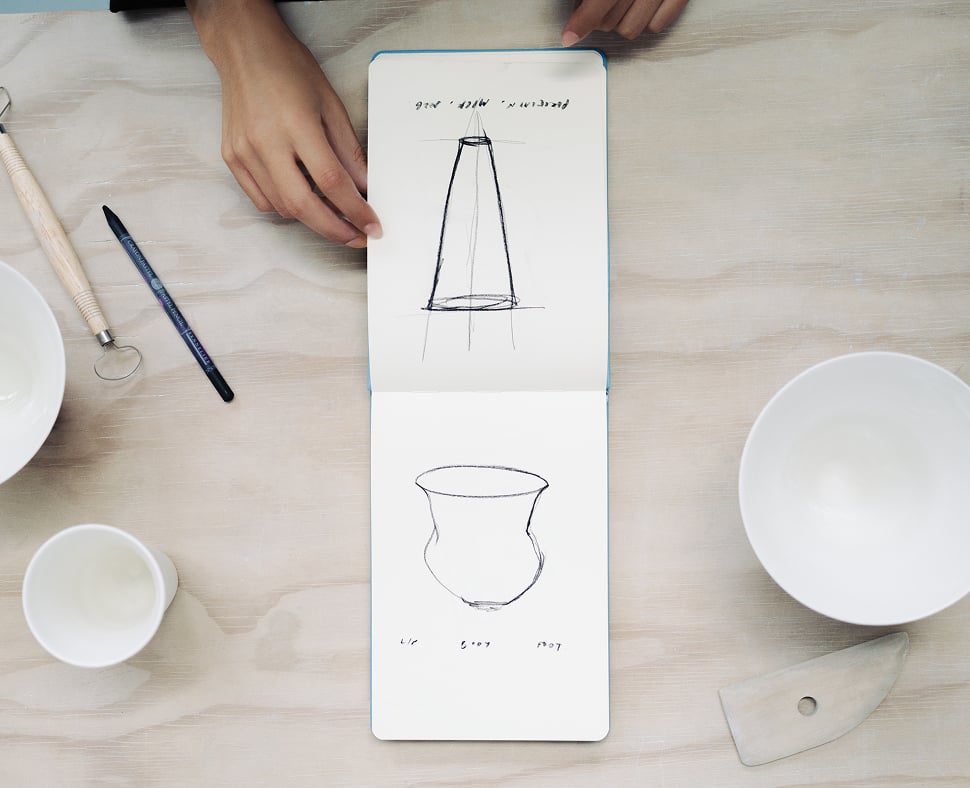 Sketchbook with vessel drawings beside ceramic bowls