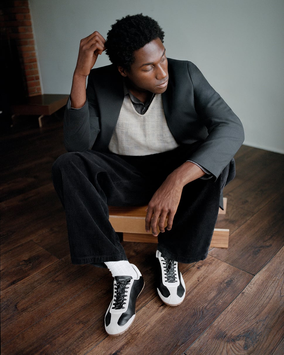 Jabari Wimbley crouched on a wooden floor wearing black and white PEDRO sneakers