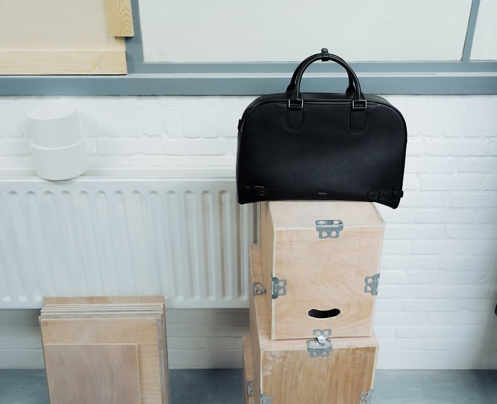 A black PEDRO bag on top of stacked cardboard boxes