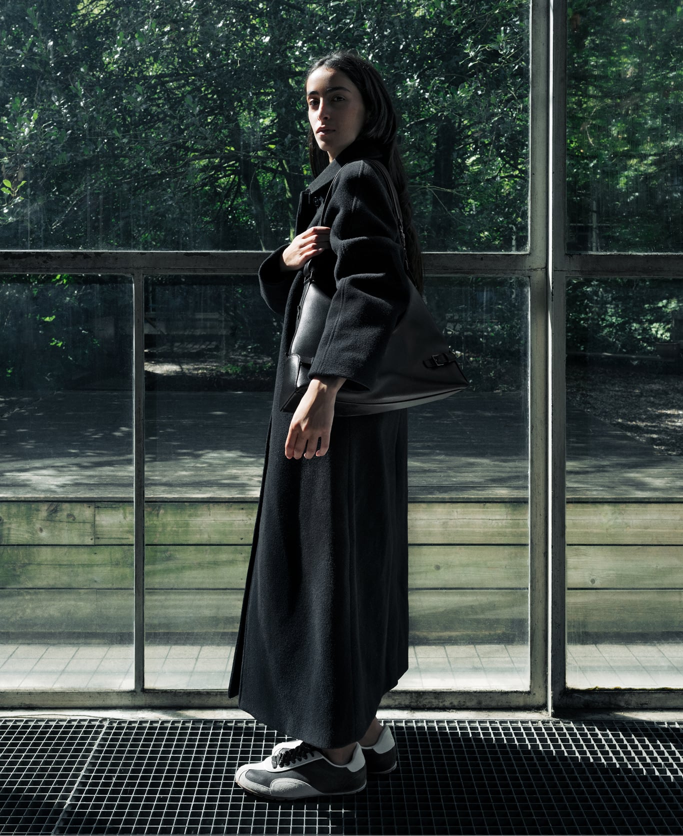 Tahni Bouhadana in a long black coat standing by a large window