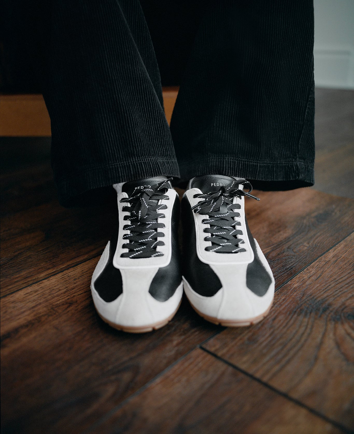 Close-up of black and white PEDRO sneakers on a wooden floor