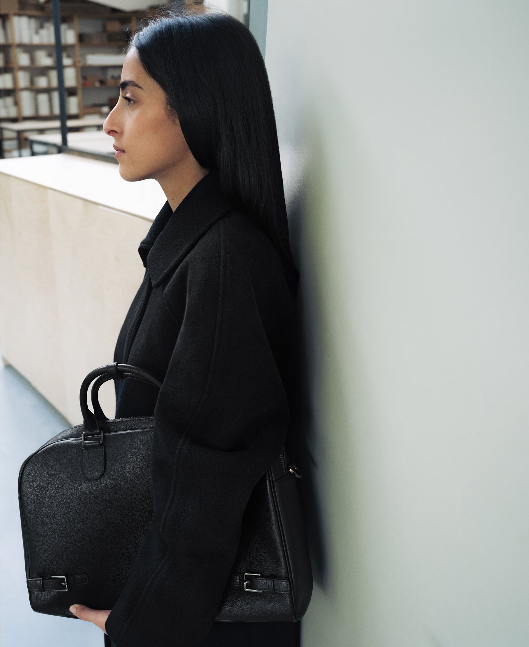 Tahni Bouhadana leaning against a white wall holding a black PEDRO bag